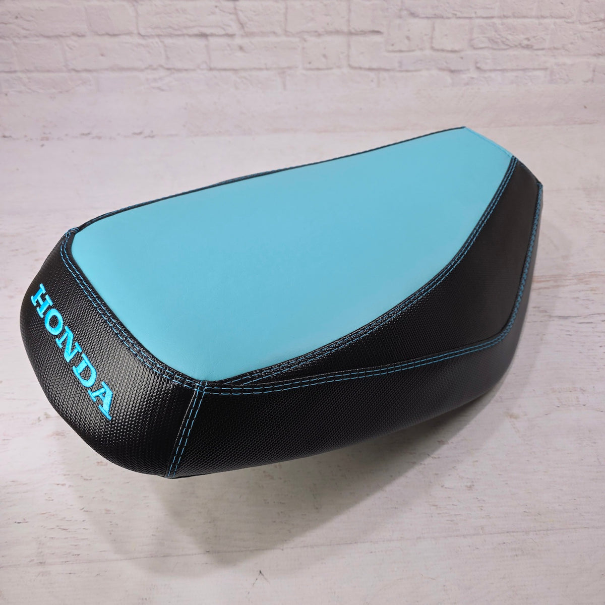 Honda Dio 1 & 2 Aqua Blue Two Tone Seat Cover with black carbon fiber sides and a blue embroidered Honda logo, handmade seat cover by Cheeky Seats