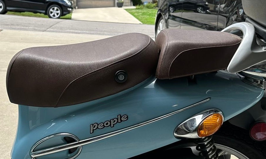 Close-up of a two-piece seat cover set on a light blue Kymco People 50, showing the driver seat and passenger pillion fitted side by side