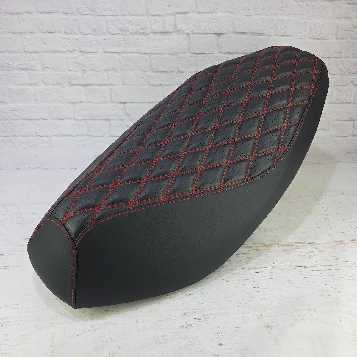 Angled view of the red-stitched Double Diamond Yamaha Zuma 50 seat cover showing its sculpted fit and smooth side panels, handmade by Cheeky Seats.