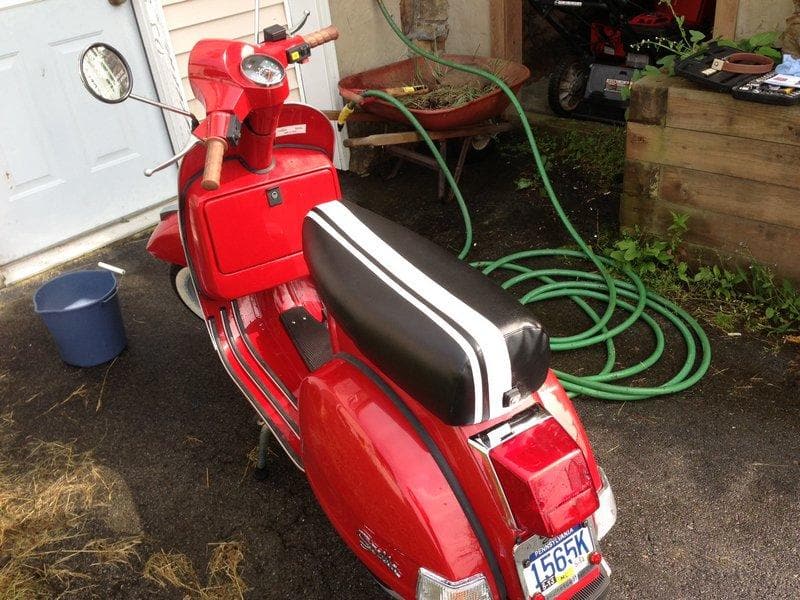 Rear view of a red Genuine Stella with a black Cheeky Seats cover and dual white racing stripes