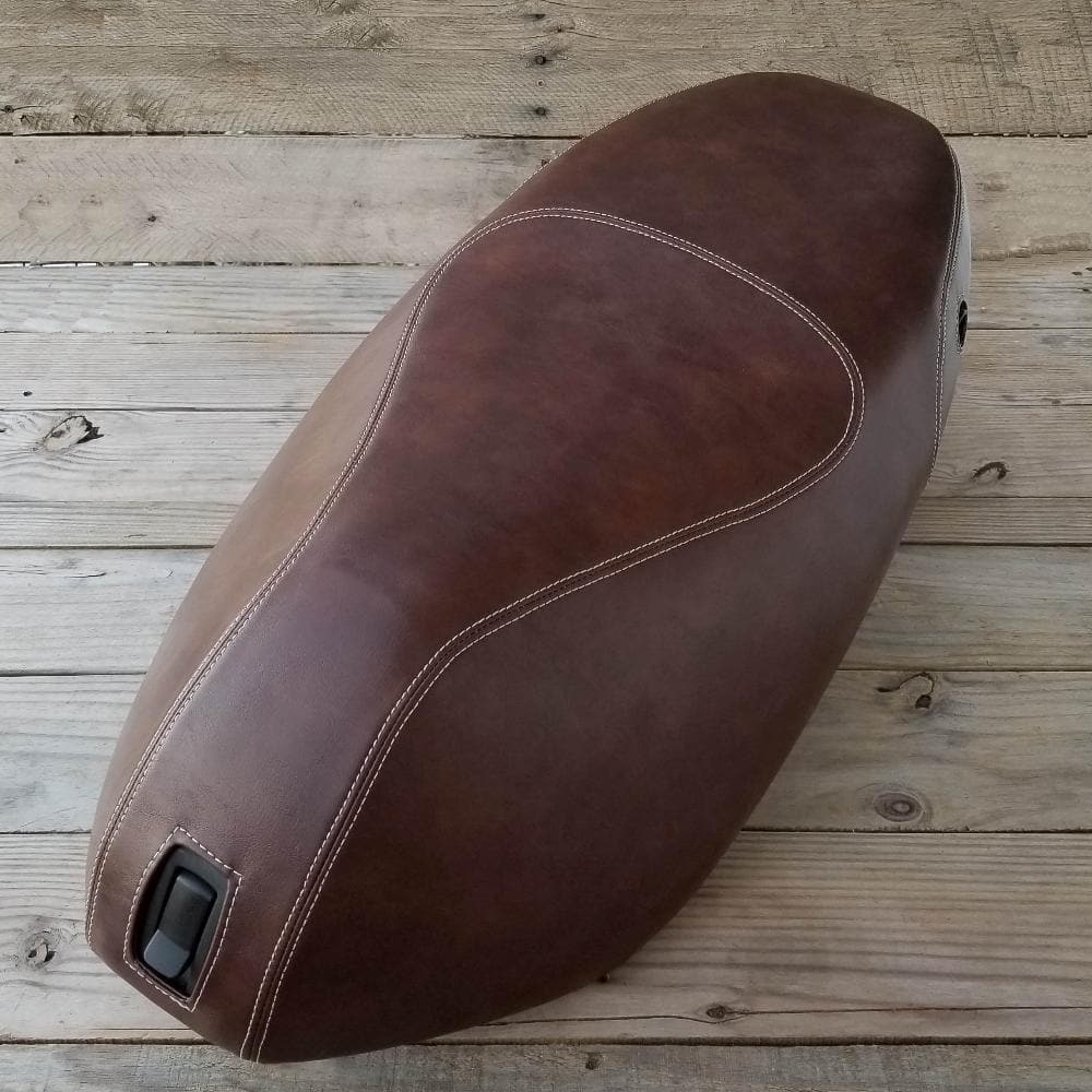 Top view of a whiskey brown Piaggio Fly seat cover with cream French seams and front lock opening, handmade by Cheeky Seats
