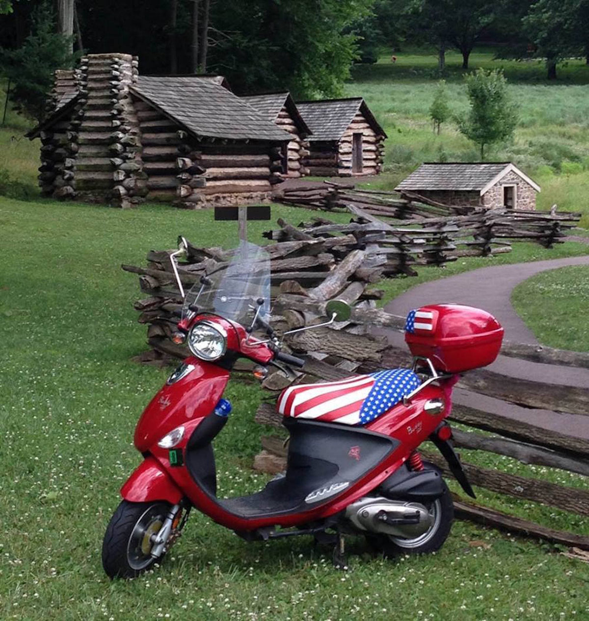 Red Genuine Buddy with an American flag Cheeky Seats cover parked by historic log cabins