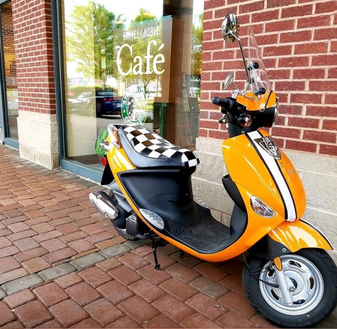Orange Genuine Buddy outside a café with a black-and-white checkered Cheeky Seats low-profile cover