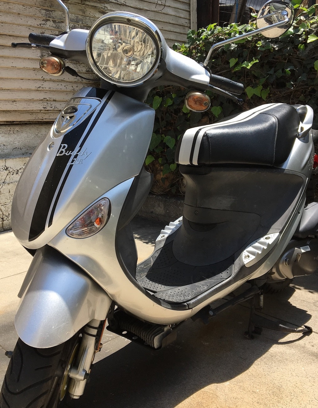 Silver Genuine Buddy with a black-and-white racing-stripe Cheeky Seats cover, front-left view