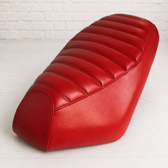 Red faux leather scooter seat cover on a brick background with tuck and roll ribs and black stitching. Handmade by Cheeky Seats