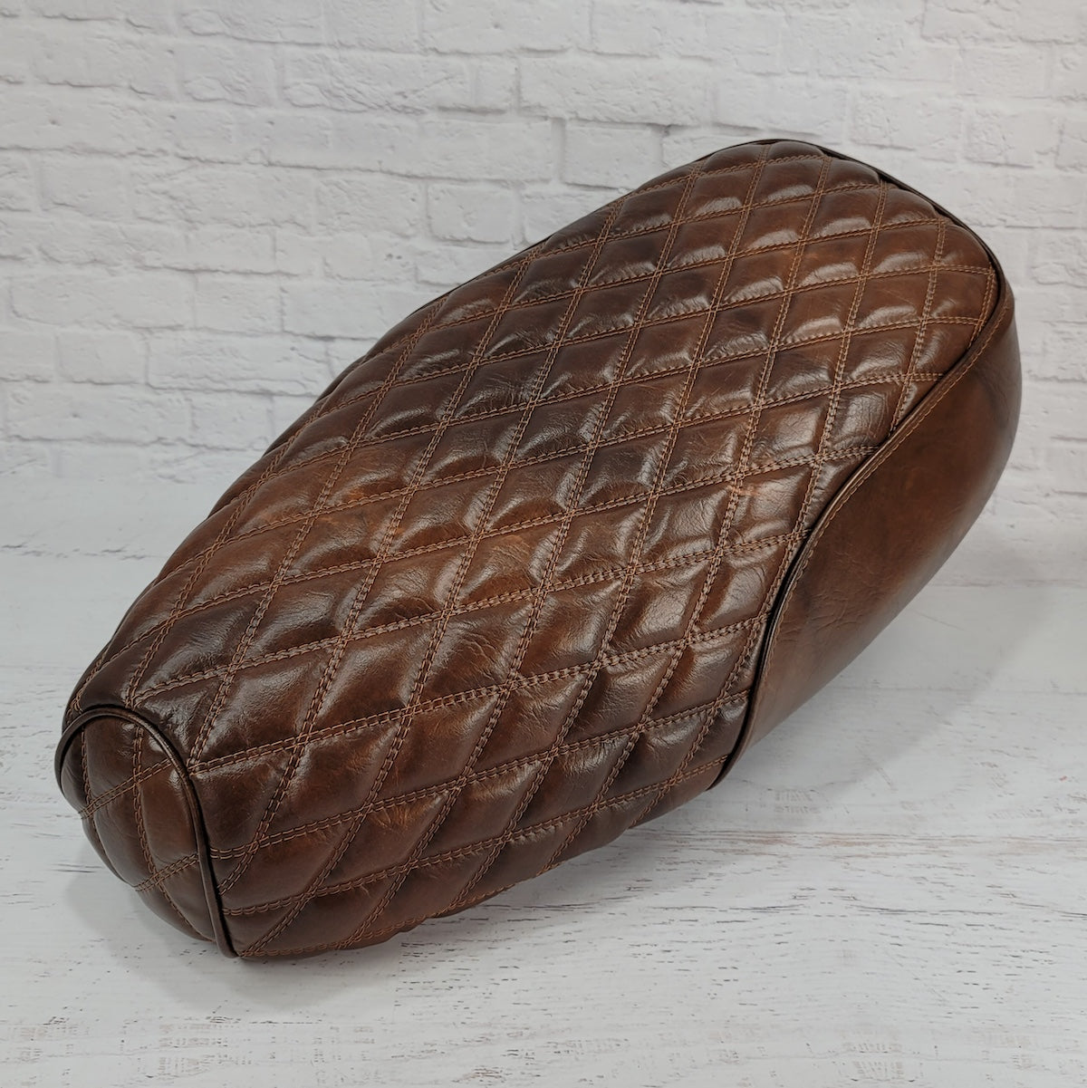 Front three-quarter view of a distressed tobacco brown Genuine Buddy Kick 125 seat cover with diamond stitching and piping,  handmade by Cheeky Seats