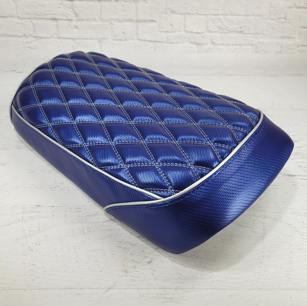 Rear three-quarter view of the carbon fiber blue diamond seat cover highlighting the white piping and textured vinyl surface, handmade by Cheeky Seats