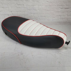 A two-tone padded seat cover for a Vespa ET, featuring black and white with red cross stitching and red piping.