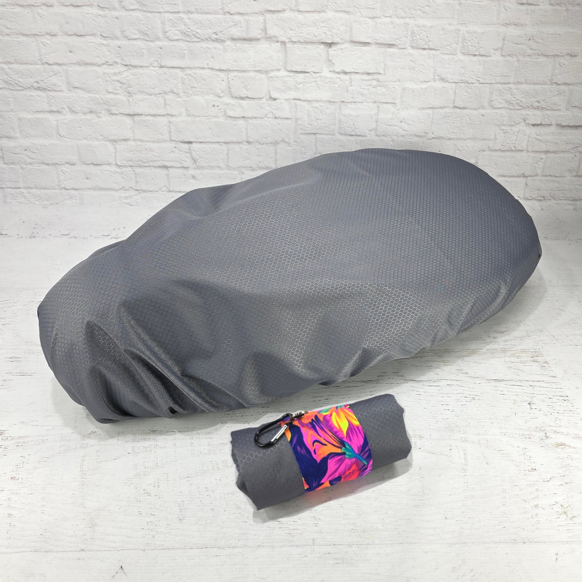 Gray honeycomb rain cover for Piaggio Fly and Liberty seats with a bright tropical carry strap and clip, by Cheeky Seats