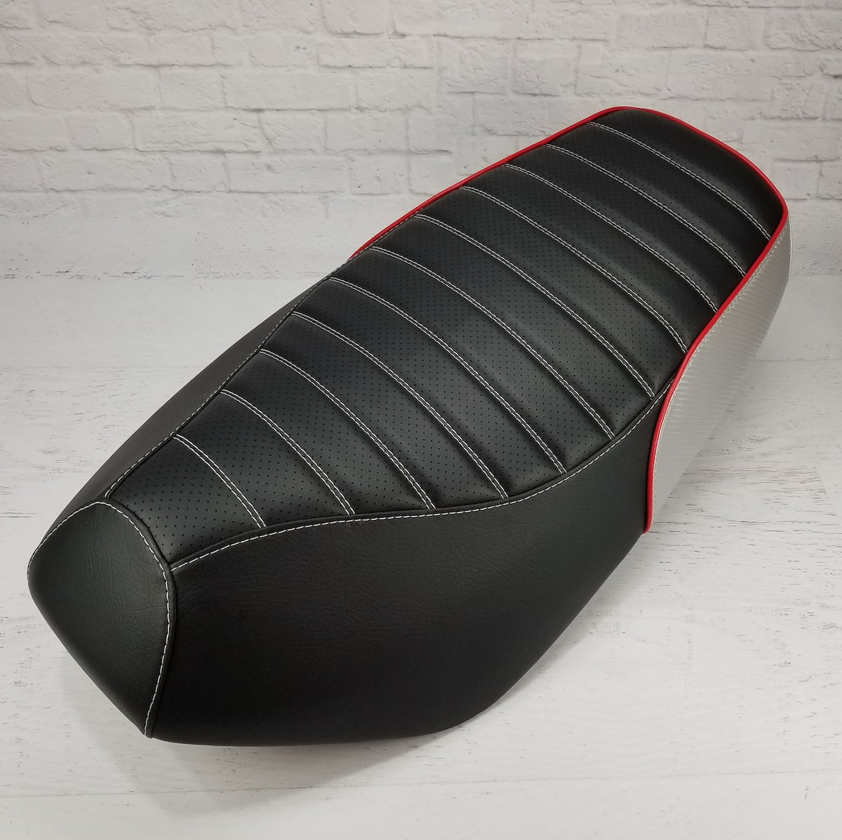 Tuck-and-roll Yamaha Zuma 50 seat cover with a perforated black top, white stitching, red piping and silver rear panel, handmade by Cheeky Seats.