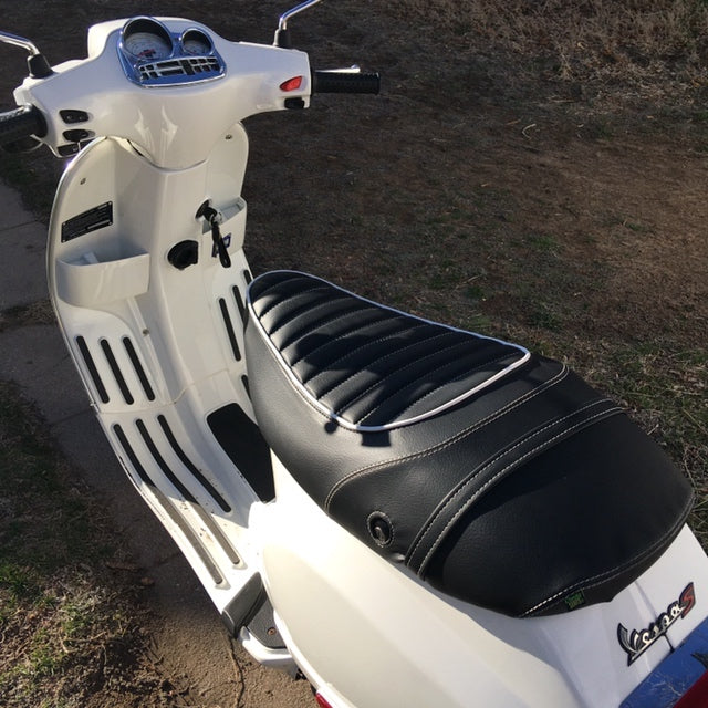 Black tuck-and-roll seat cover with light piping installed on a white Vespa S by Cheeky Seats