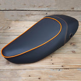 Matte black Vespa S sport-saddle seat cover with orange piping and stitching, handmade by Cheeky Seats