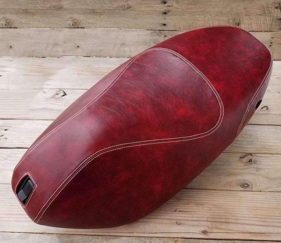 Angled view of an oxblood Piaggio Fly seat cover with cream French seams and rich marbled shading, handmade by Cheeky Seats
